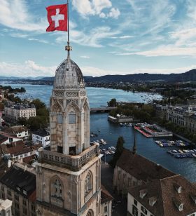 a large building with a flag on top and a body of water in the background